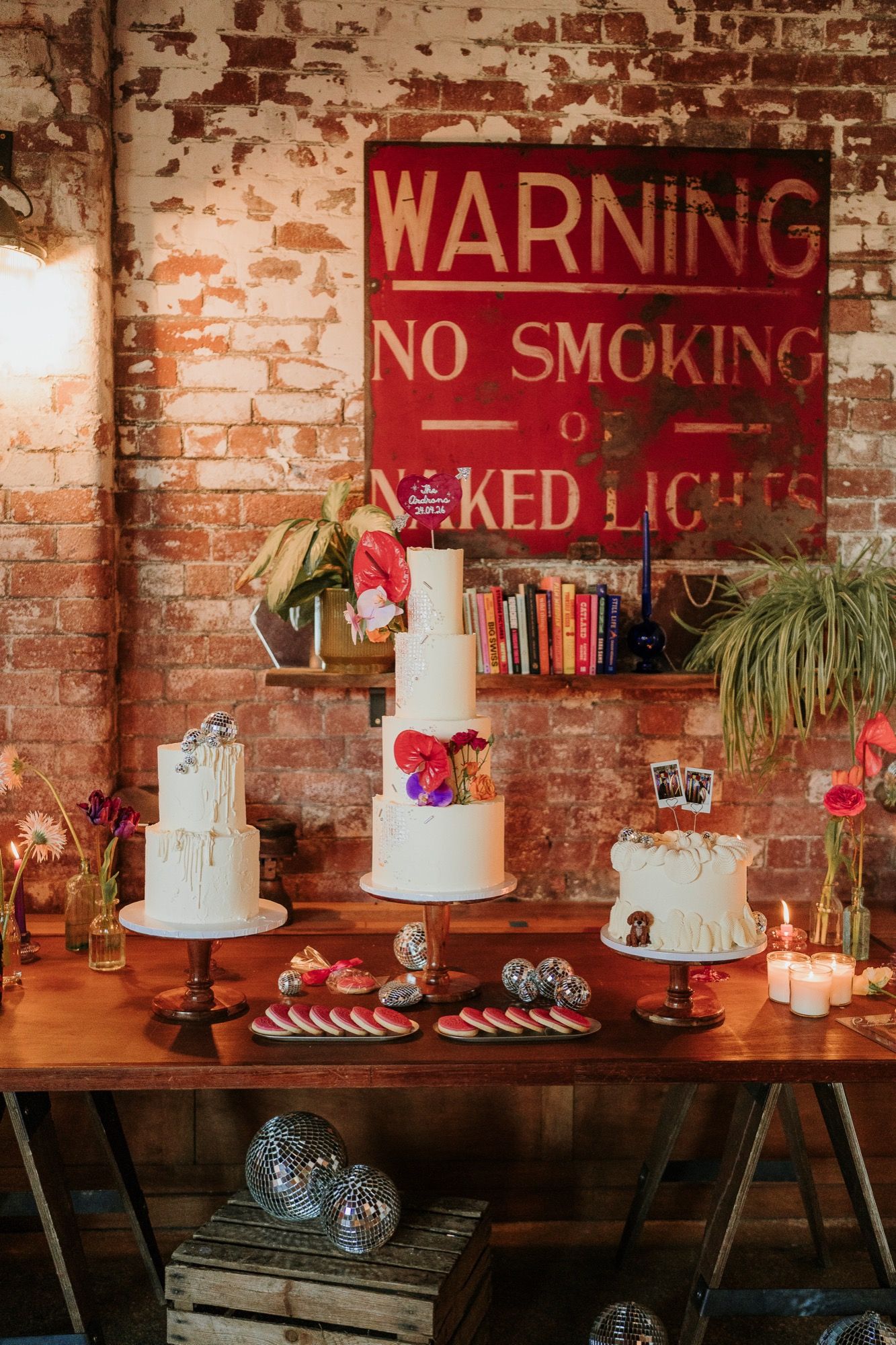 Wedding dessert table with three buttercream cakes, fresh anthuriums, disco balls and a vintage warning sign at an industrial Yorkshire venue